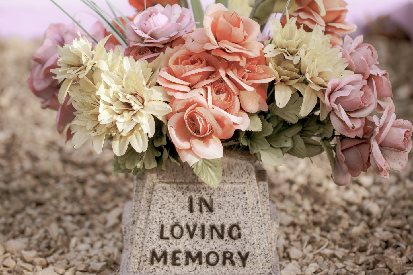 Stone memorial vase with pastel flowers reads 'In Loving Memory'.
